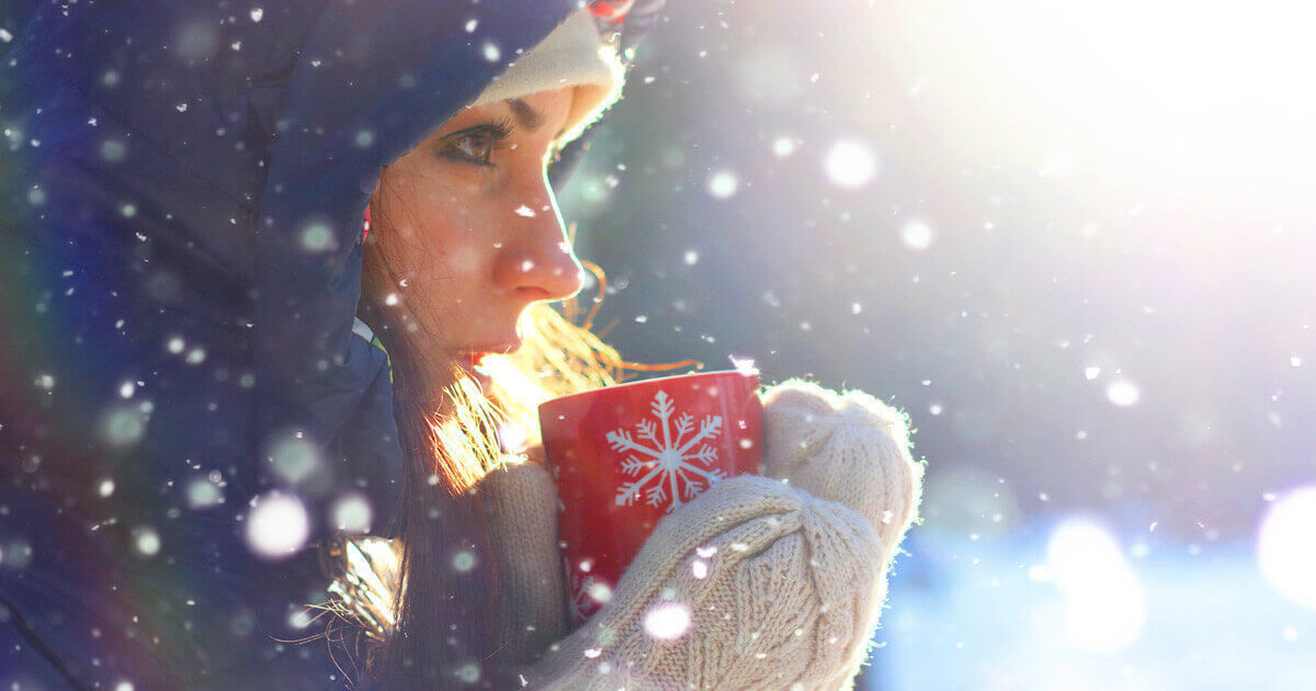 Woman in a winter hood holding a warm mug in the snow