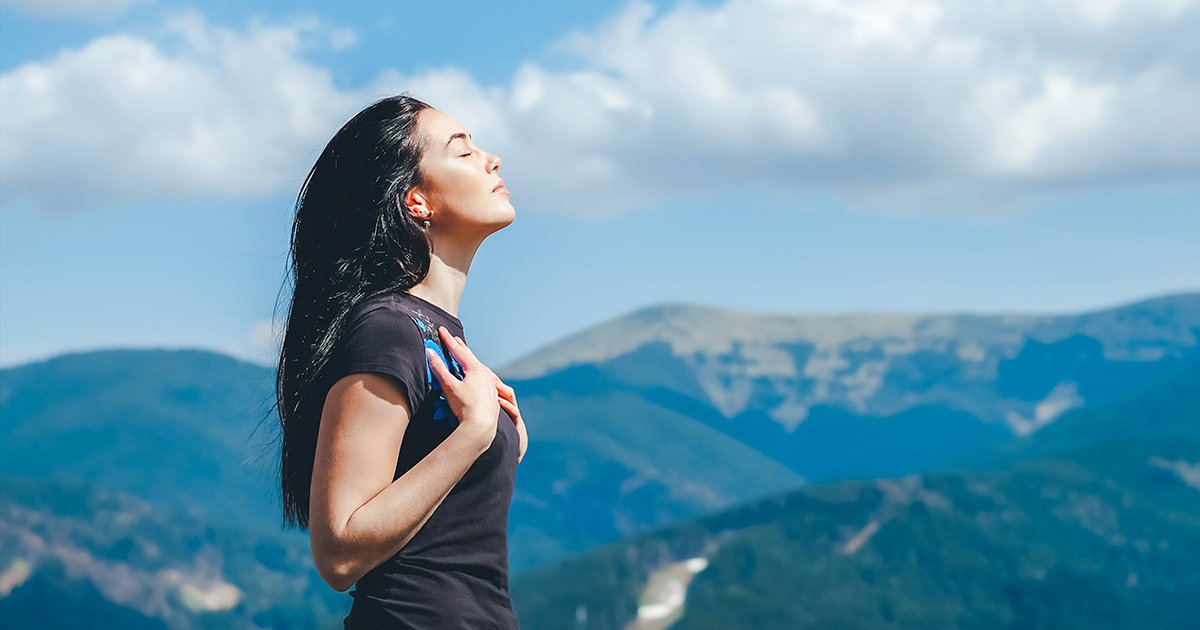 woman doing breath work with surrounding mountain vistas